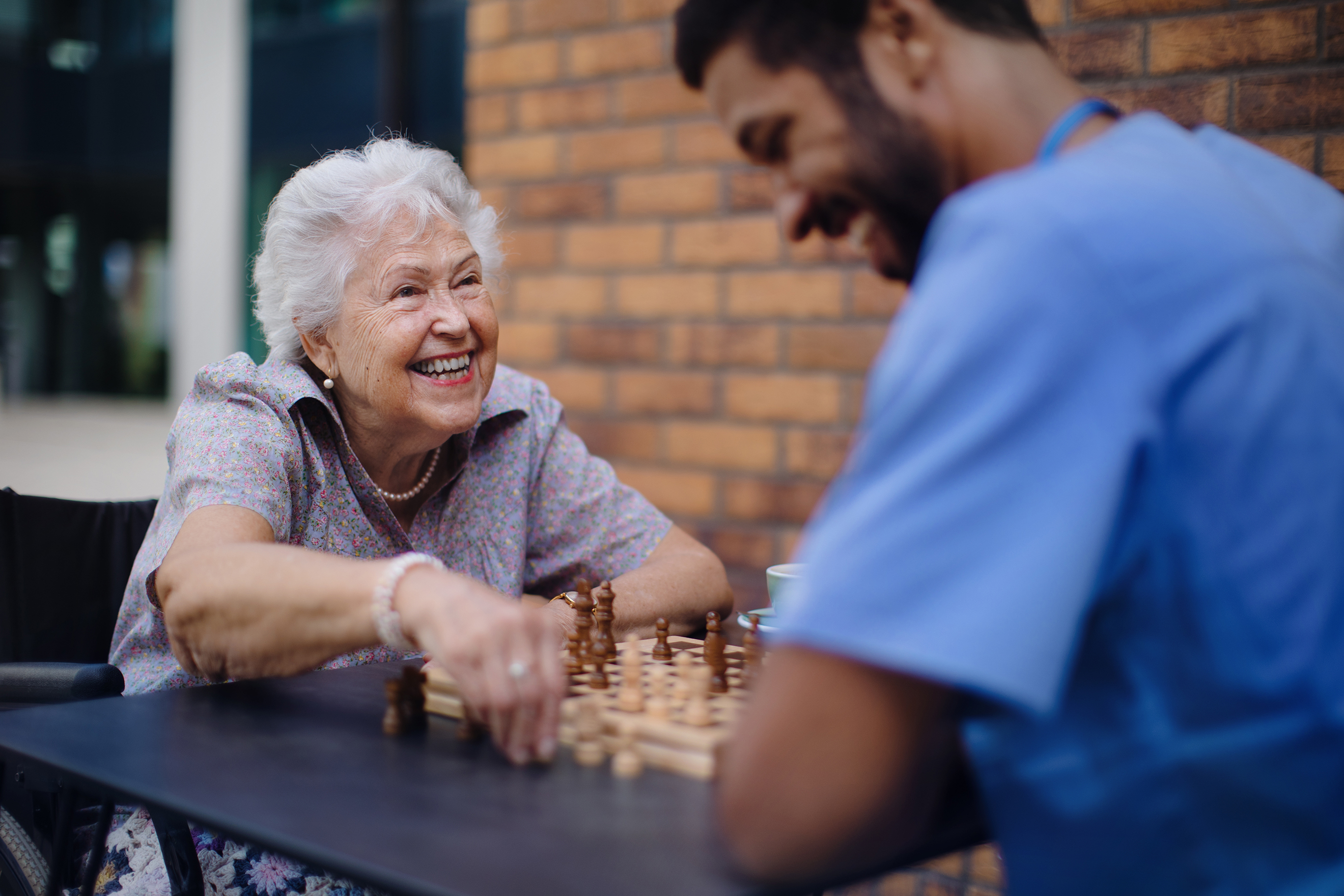 caregiver playing chess and drinking coffee with an elderly lady 